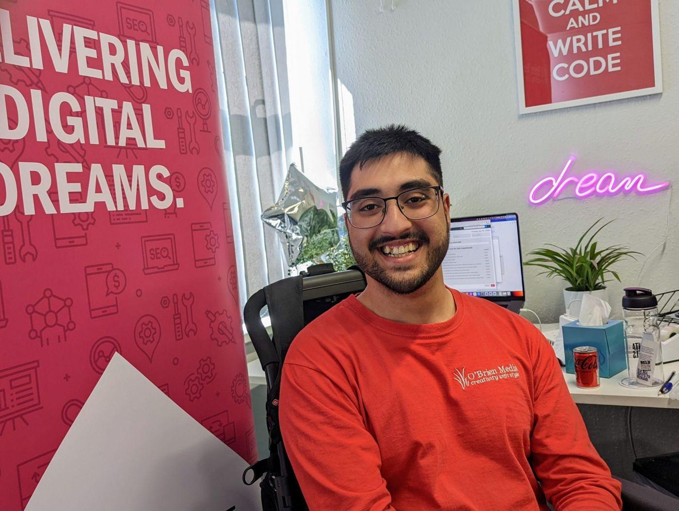 Camilo Pires, O’Brien Media Inclusion Officer, smiling at his desk in the office