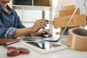 Two business owner are working together to pack products and check customers' orders on their laptops at home