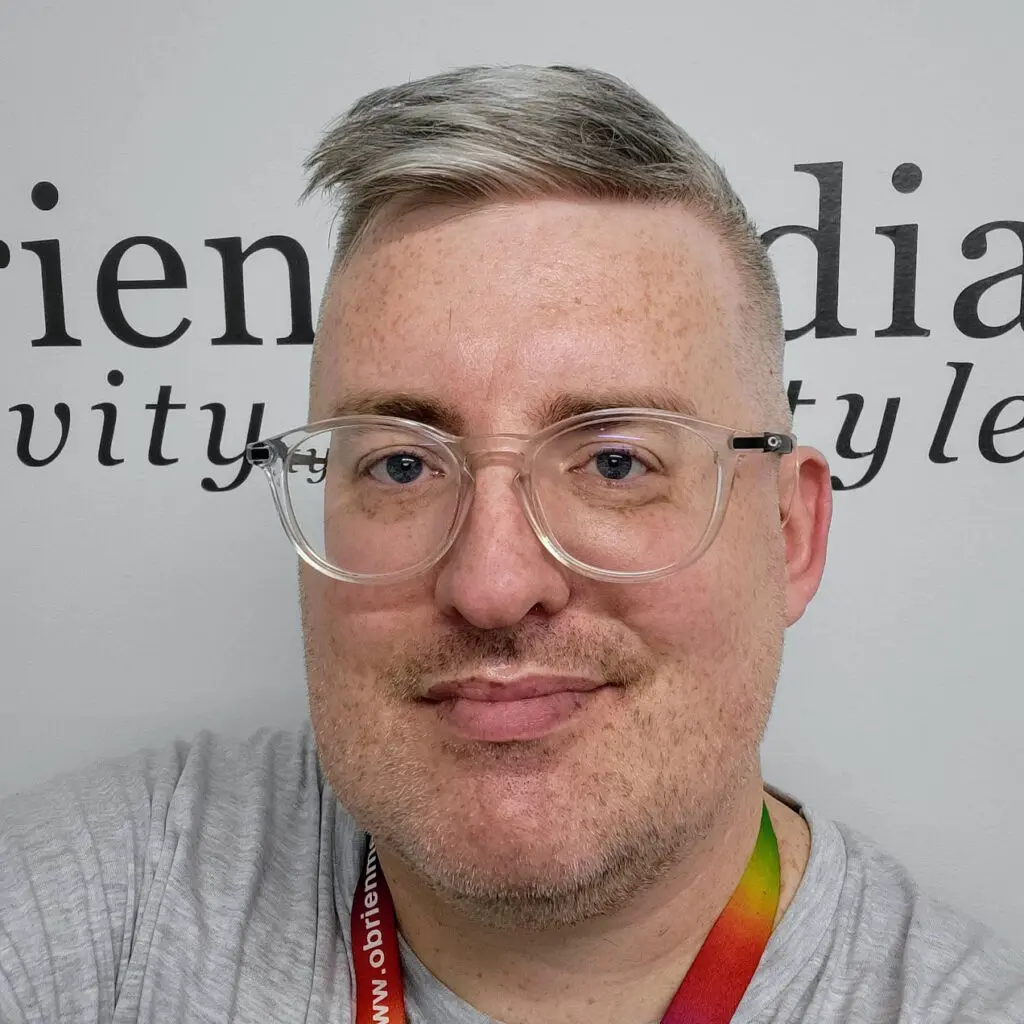 Chris, Head of Design & Development at O’Brien Media, wearing glasses and a rainbow lanyard