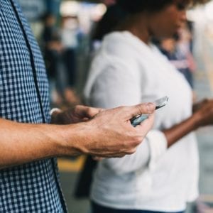 two persons using mobiles and waiting on a rail station