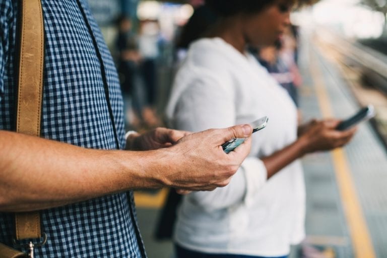 two persons using mobiles and waiting on a rail station