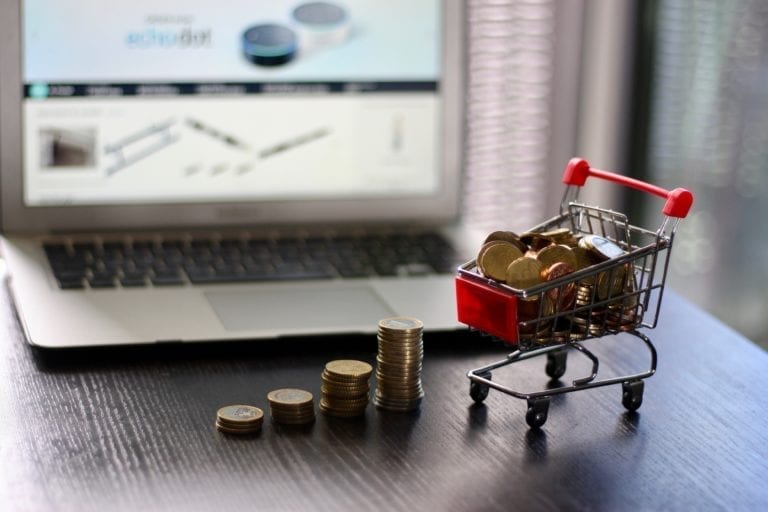 small shopping cart full with coins and a laptop