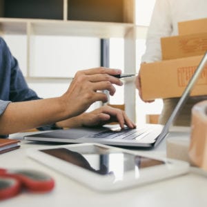 Two business owner are working together to pack products and check customers' orders on their laptops at home