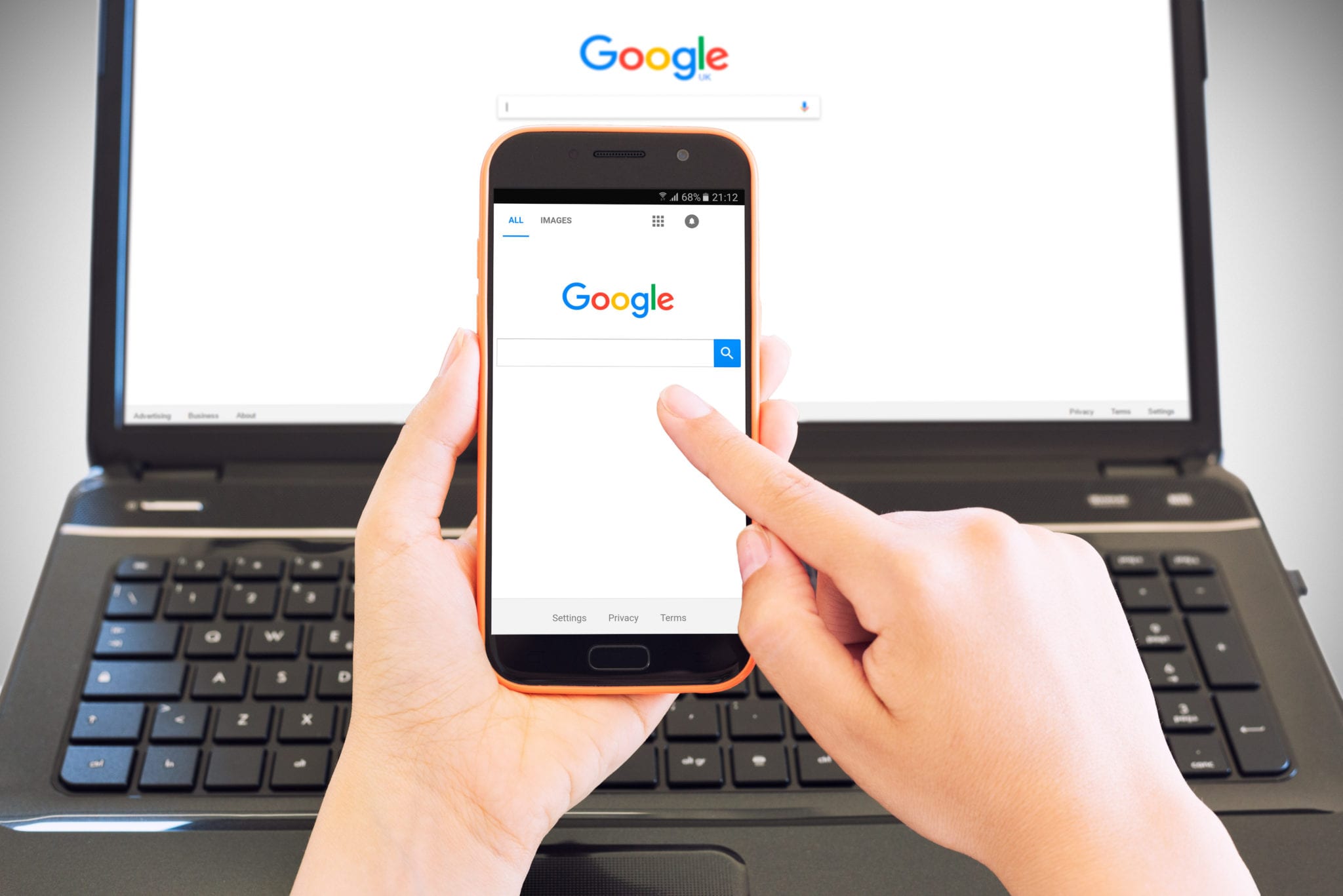 Smartphone on female hands browsing Google Home Page and in background a portable computer with the same site