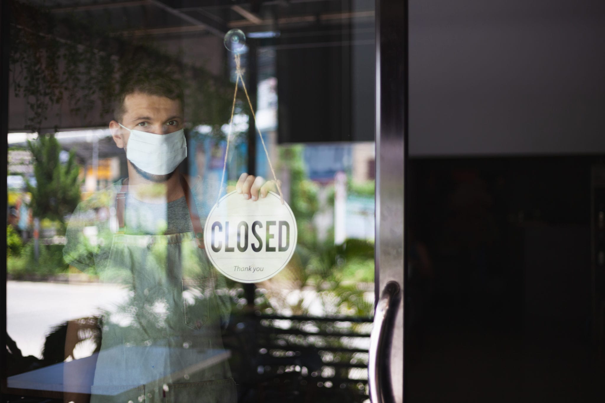 Chef in safety mask hanging up sign closed on restaurant door