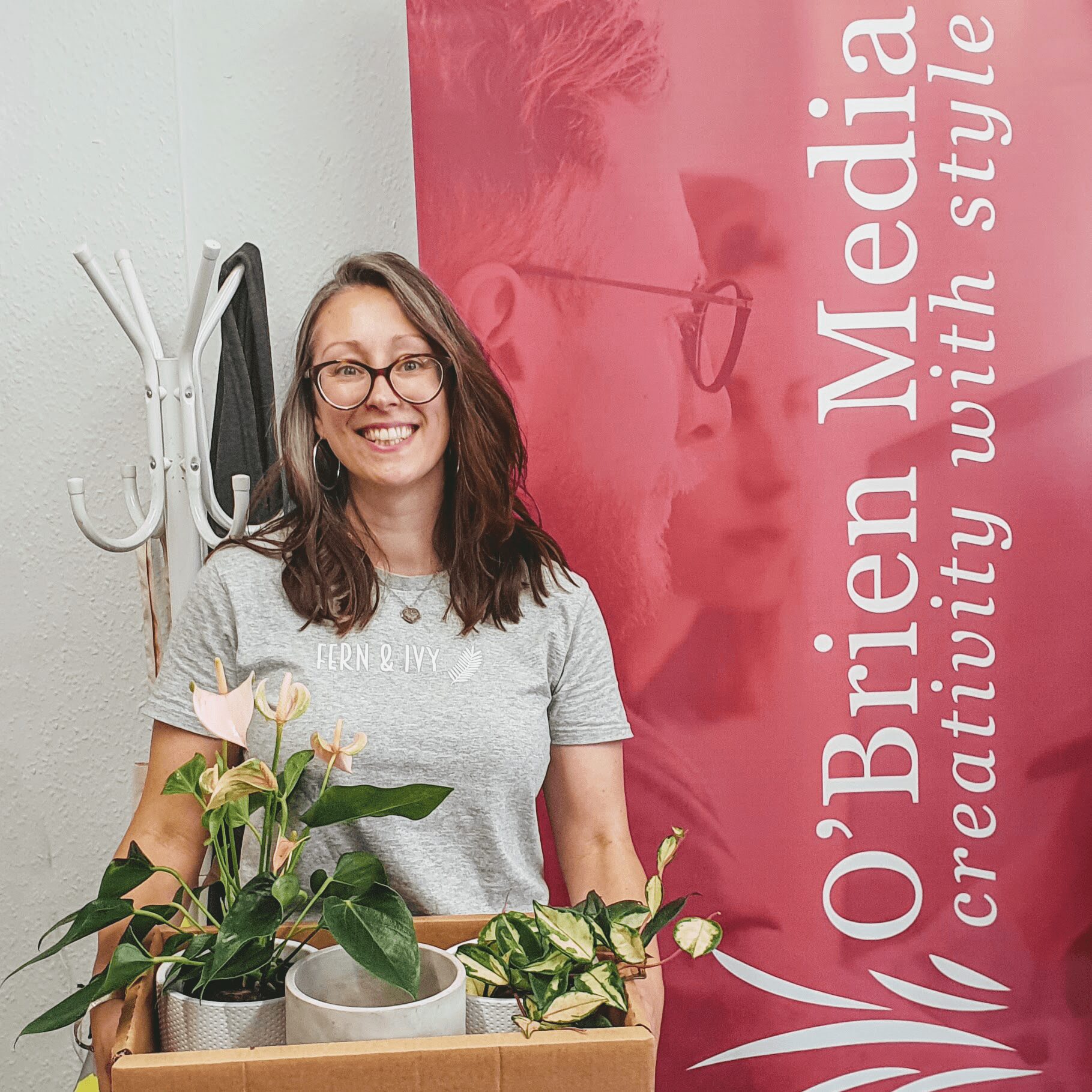 A woman with plants in fron of a OBrien Media banner
