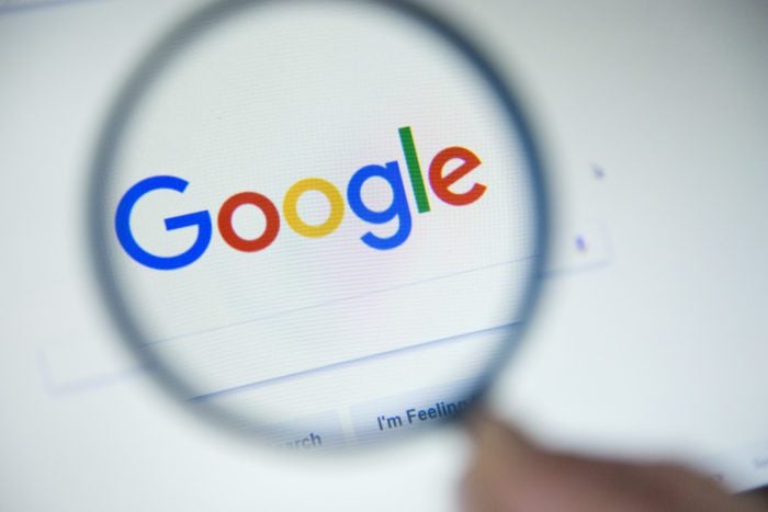 Google homepage on the screen under a magnifying glass.