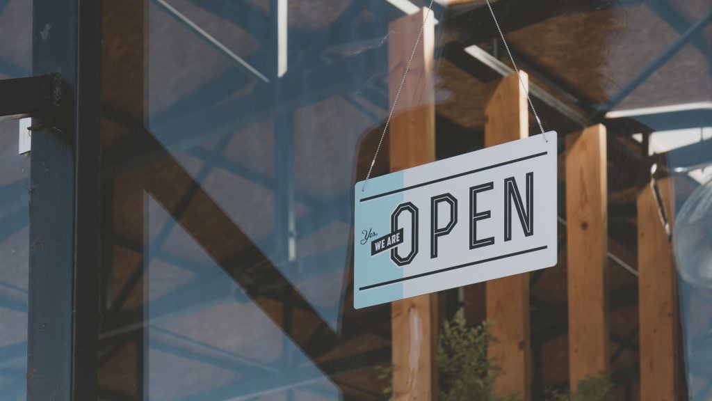 A close-up of a modern “We Are Open” sign hanging inside a shop window