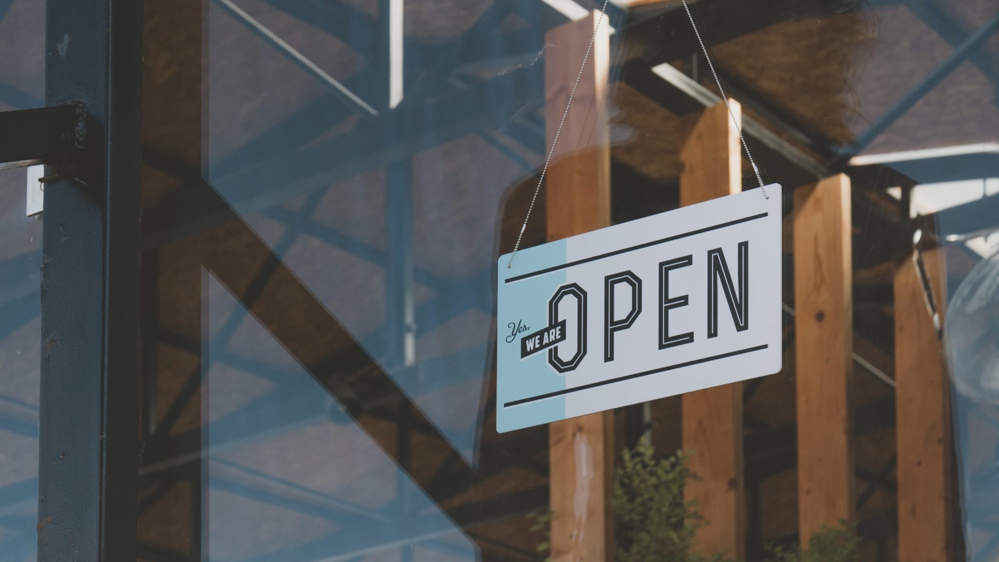 A close-up of a modern “We Are Open” sign hanging inside a shop window