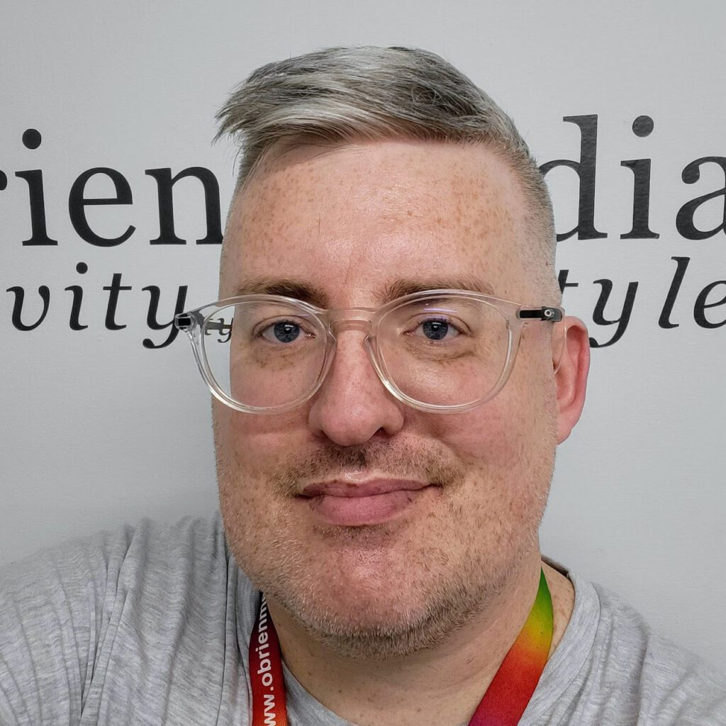 Chris, Head of Design & Development at O’Brien Media, wearing glasses and a rainbow lanyard
