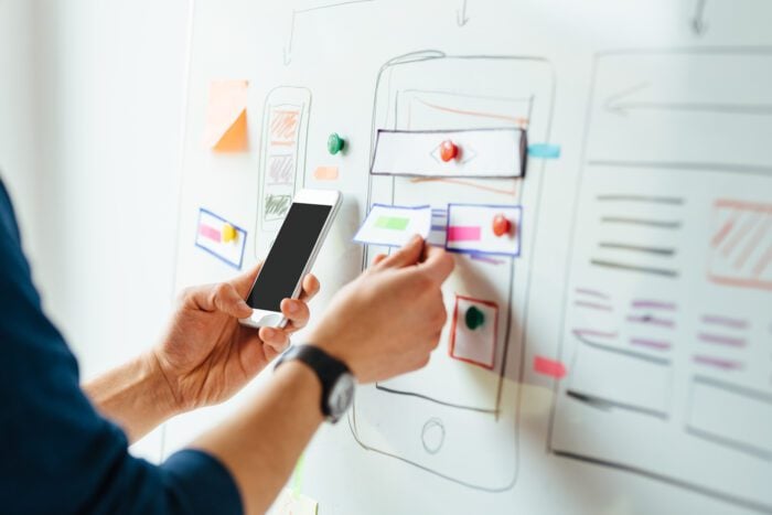 Person holding a smartphone and planning animated website interface on a whiteboard