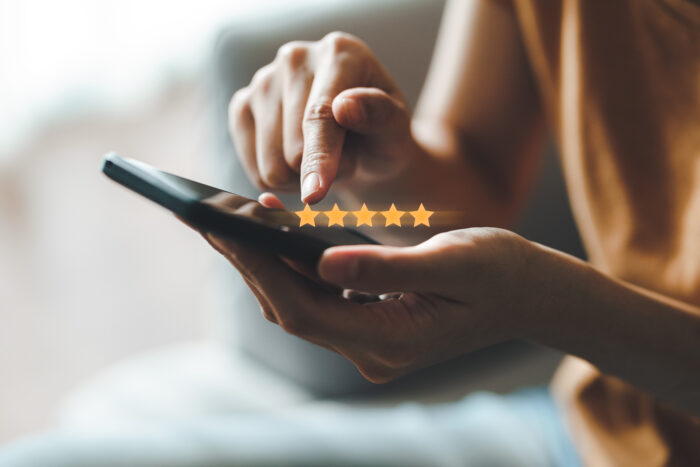 Hand interacting with smartphone screen to leave a five-star rating, symbolising online customer feedback