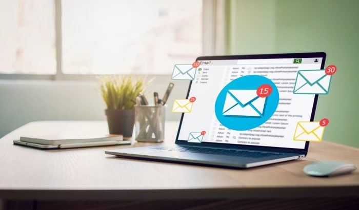 Laptop on a desk showing an email inbox with multiple message notifications popping out of the screen