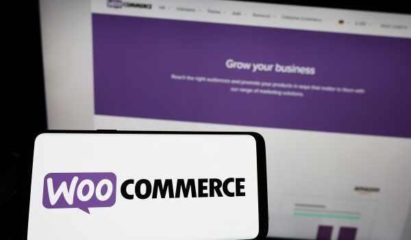Stuttgart, Germany - 12-02-2022: Person holding cellphone with logo of open-source e-commerce solution WooCommerce on screen in front of business webpage. Focus on phone display.