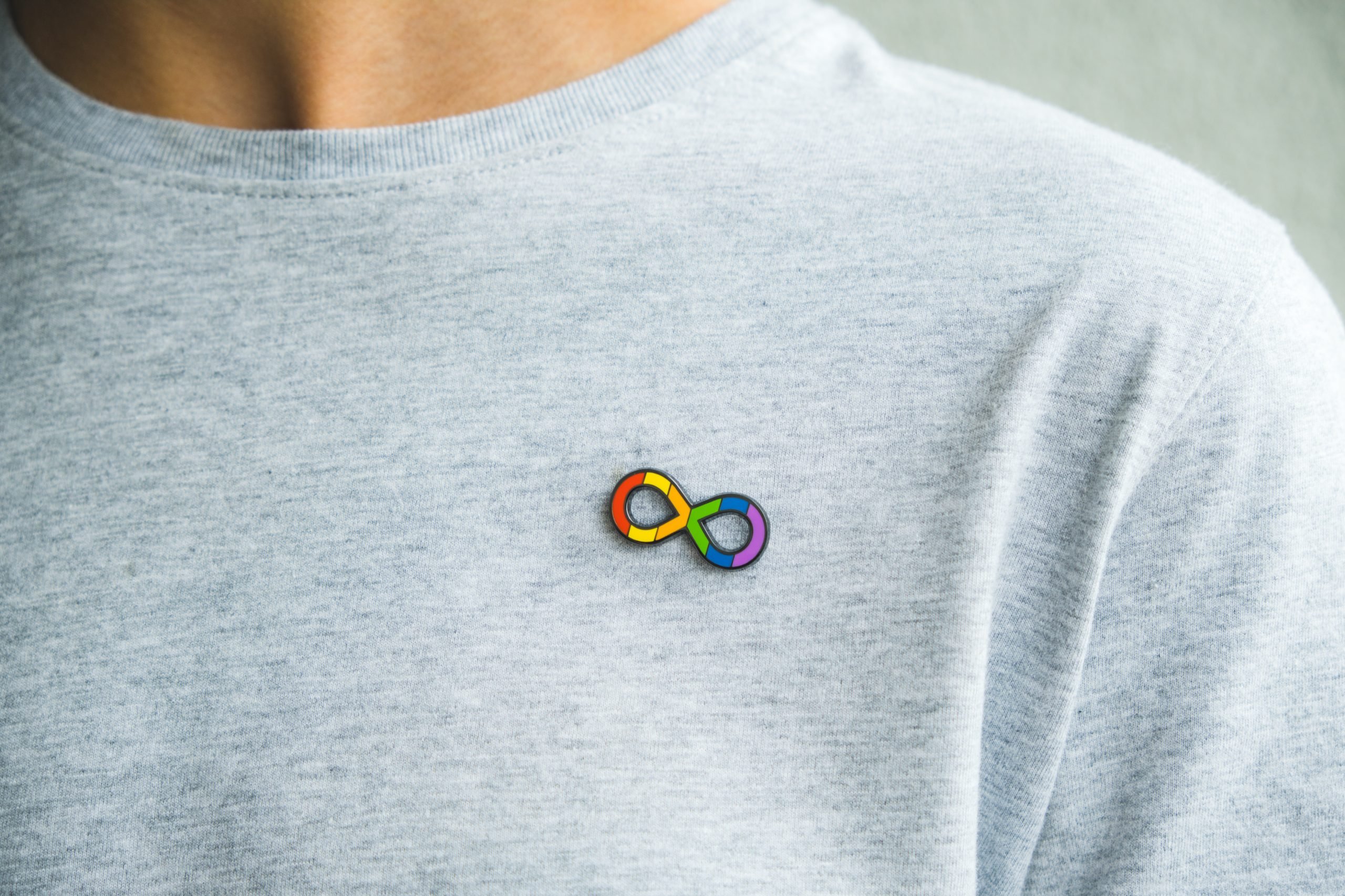 Teenage boy with autism infinity rainbow symbol sign metallic pin brooch on t-shirt. World autism awareness day, autism rights movement, neurodiversity, autistic acceptance movement.