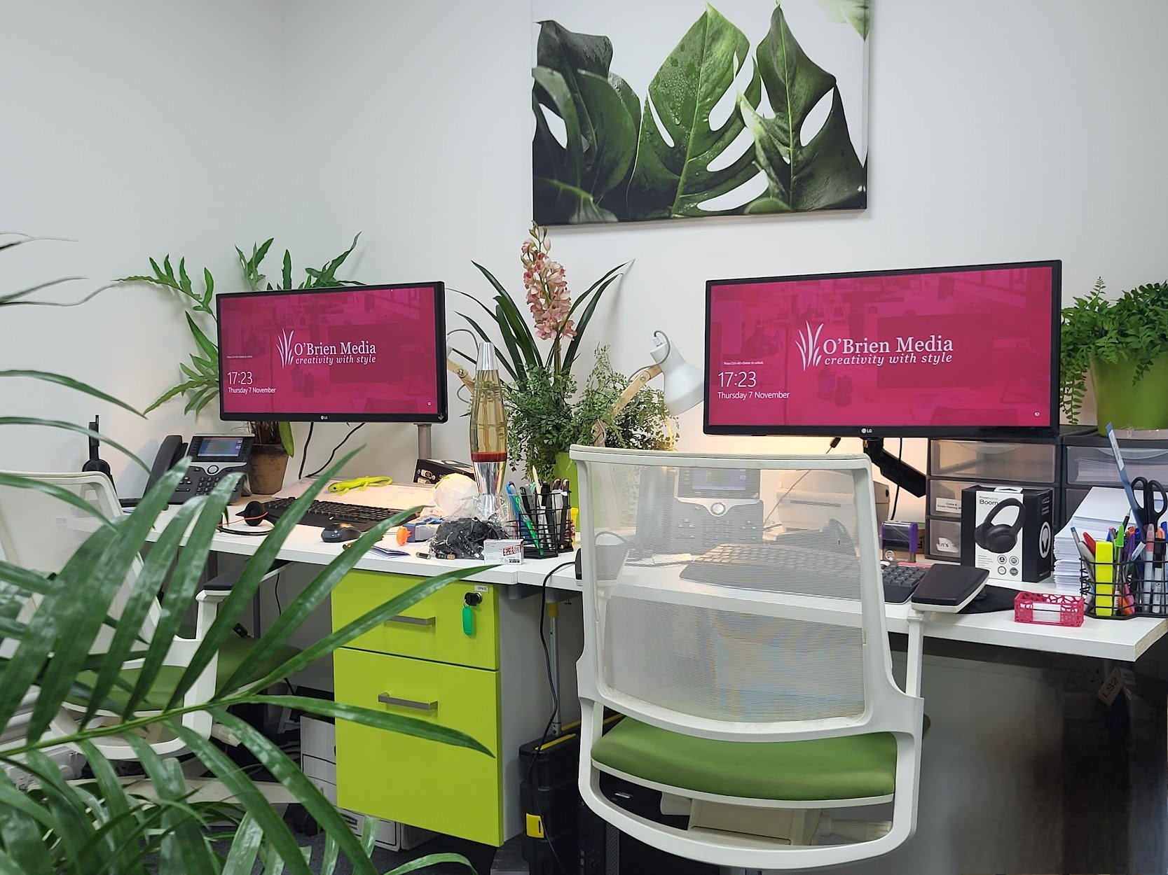 A photo of two white desks in the O'Brien Media offices with pink screensaver images amongst green plants.