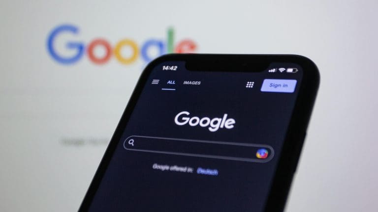 Gogle on a screen behind a smartphone also displaying the Google search screen