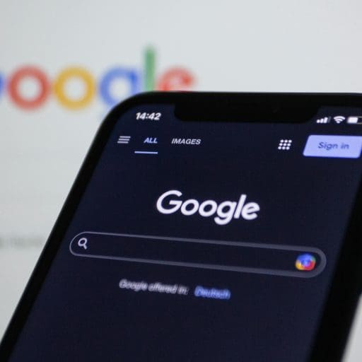 Google on a screen behind a smartphone also displaying the Google search screen