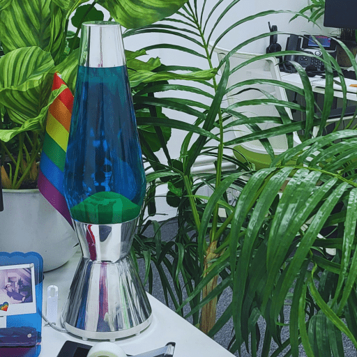 Blue and green lava lamp on desk in O'Brien Media office surrounded by plants and a pride flag