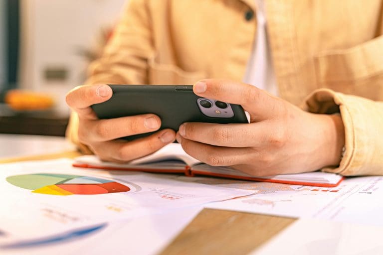 Person checking a phone with data reports on desk, representing digital update management